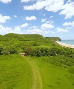a green hill with a dirt road next to the beach at Villa Del Carmen Family Vacation Home in Isabela