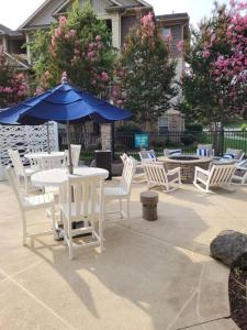 eine Terrasse mit weißen Tischen und Stühlen und einem blauen Sonnenschirm in der Unterkunft South Charlotte’s Cozy & Modern in Charlotte
