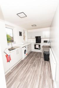 a kitchen with white cabinets and a wooden floor at Greenbourne - 4 bedrooms Sleeps 8 free parking in Gateshead