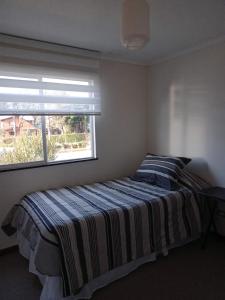 1 dormitorio con 1 cama con manta a rayas y ventana en Casa Condominio Los Robles II Púcon, en Pucón