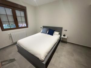 um quarto com uma cama com lençóis brancos e almofadas azuis em APARTAMENTOS EL ROJU em Santillana del Mar