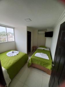 a bedroom with two beds with green sheets and a window at Hotel Gloria Del Norte in Cartagena de Indias