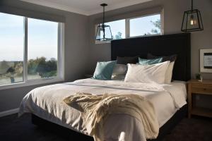a bedroom with a bed with white sheets and windows at Quartz Retreat in Daylesford