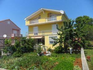 ein gelbes Haus mit einem Balkon und Bäumen in der Unterkunft Apartments Marina in Sukošan