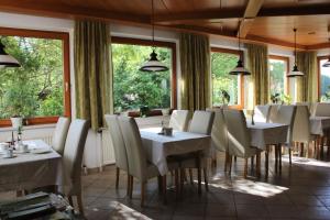 un restaurante con mesas y sillas blancas y ventanas en Gasthof-Pension Zum Haugstein - Familie Eder, en Engelhartszell