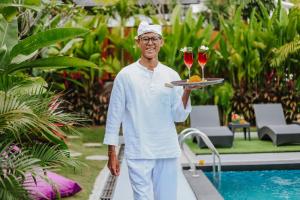 un homme tenant un plateau avec deux verres de vin dans l'établissement Le Cielo Resort Umalas by Maviba, à Canggu