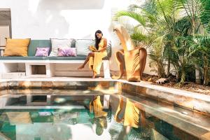 a woman sitting on a couch next to a swimming pool at Guest House et Restaurant Sous le Badamier in Grand Baie