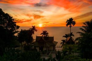 a sunset over the ocean with a house and palm trees at Ayara Kamala Resort & Spa in Kamala Beach
