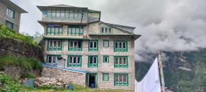 un grand bâtiment en briques avec des fenêtres vertes sur une colline dans l'établissement Hotel hillten, à Namche