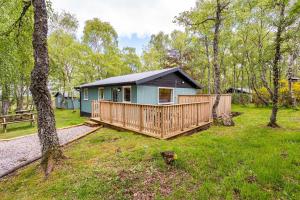 a small blue house with a deck in a yard at Heather Lodge 3 with Hot Tub in Belladrum