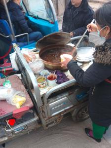 a woman is cooking food in a food cart at Pingyao hu lu wa Home Inn in Pingyao