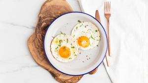 two eggs in a bowl on a wooden plate with a fork at Wildlife Resort Jim Corbett in Kālāgarh