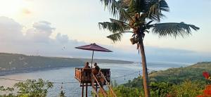 Dos personas sentadas bajo un paraguas en un balcón con vistas al océano en Gamat Garden Homestay en Nusa Penida