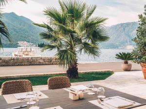 einen Tisch mit Stühlen und eine Palme neben dem Wasser in der Unterkunft Heritage Grand Perast By Rixos in Perast