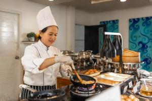 a woman in a kitchen preparing food in a wok at Centara Kata Resort Phuket in Kata Beach