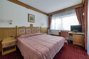 a bedroom with a bed and a desk and a television at Alpenhotel Panorama in Campitello di Fassa