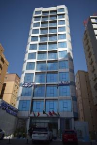 wysoki budynek z samochodami zaparkowanymi przed nim w obiekcie Atlantis Suites Hotel w Kuwejcie