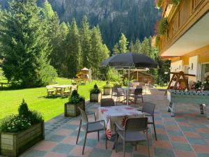 un patio con tavoli, sedie e ombrellone di Alpenhotel Panorama a Campitello di Fassa