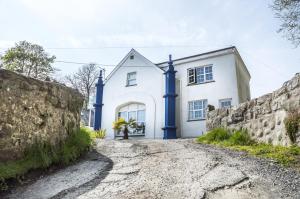 a white house with blue columns on a stone wall at The Coach House - 3 Bedroom Holiday Home - Penally - Tenby in Penally