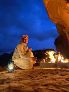 a man sitting in front of a fire at Wadi Rum Originality Camp in Wadi Rum