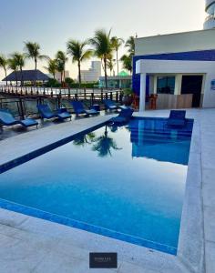 a swimming pool with blue chairs and palm trees at PRAIA DE MUCURIPE - FRENTE MAR - Ap205 in Fortaleza