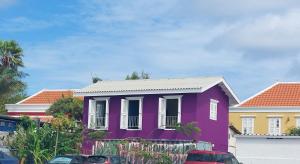 Purple house in colorful city centre في فيليمستاد: منزل ارجواني فيه سيارات تقف امامه