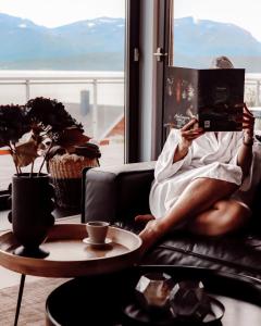 une femme assise sur un canapé qui lit un livre dans l'établissement Malangen Resort, à Mestervik