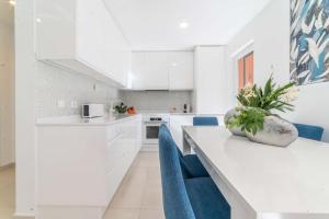 uma cozinha com armários brancos e uma mesa com cadeiras azuis em Apartment Aroeira Green Jodi em Aroeira