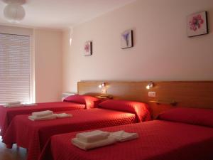 two beds in a room with red sheets and towels at Pensión A Solaina in O Pedrouzo