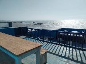 uma mesa e um banco num deque com vista para a água em La Maison des Artistes em Essaouira