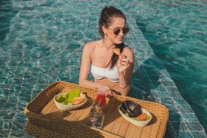 a woman sitting in a swimming pool with a tray of food at Pousada Corália in São Miguel dos Milagres