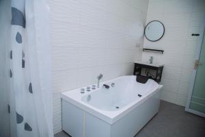 ein weißes Bad mit einer Badewanne und einem Spiegel in der Unterkunft VEGAS LUXURY HOTEL in Daressalam