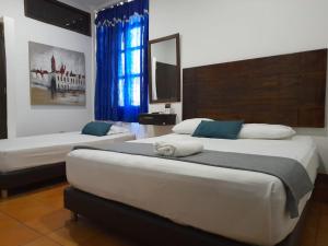a bedroom with two beds and a window with blue curtains at hotel san nicolas colonial in Barranquilla