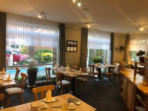 un restaurante con mesas y sillas de madera y ventanas en Garni Hotel-Pension Holum, en Neuharlingersiel
