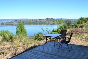 a table and two chairs sitting on a deck next to a lake at Cabaña mirador Quento in Quilquico