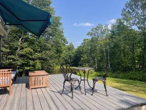a deck with two chairs and a table and an umbrella at Not-so-tiny, Tranquil, Pond front Bungalow in Canaan