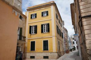 um edifício amarelo com quatro janelas numa rua em Es Mirador Hotel em Ciutadella