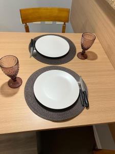 dos platos blancos y dos vasos sobre una mesa de madera en FLAT no Gonzaga com estacionamento incluso en Santos