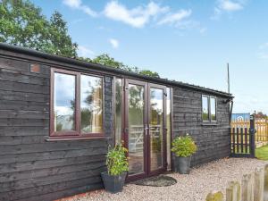 une petite maison noire avec des portes en verre et des plantes en pot dans l'établissement Newlyn Cottage, à Pluckley
