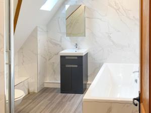 a white bathroom with a sink and a bath tub at Ringland Cottage in Attlebridge