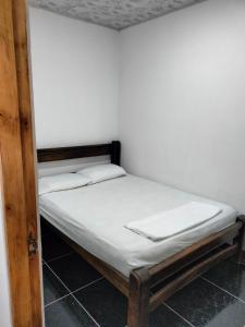 Cama pequeña con sábanas blancas y marco de madera en Apartamento, La paz, en Puerto Triunfo