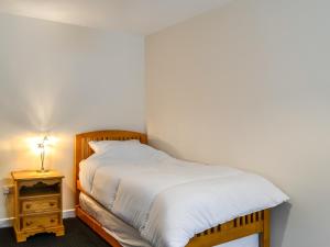 um quarto com uma cama com lençóis brancos e uma mesa de cabeceira em The Hydeaway em Whithorn