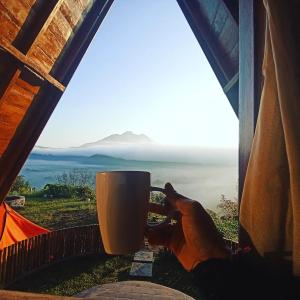 a person holding a cup of coffee in front of a window at Kintamani Adventure 'The Hideway in Kintamani' in Kintamani