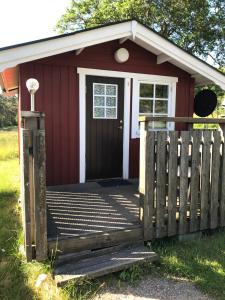 einen roten Schuppen mit einer Veranda und einer Tür in der Unterkunft Björsjöås Vildmark - Small camping cabin close to nature in Olofstorp