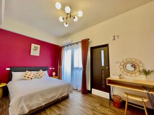 1 dormitorio con pared roja, cama y escritorio en Mian Bao Homestay en Magong