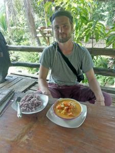 un hombre sentado en una mesa con un plato de comida en Easylife Bungalow en Ko Lanta