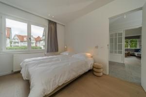 een witte slaapkamer met een bed en een groot raam bij Le Calme des Dunes in Koksijde