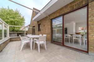 een patio met witte stoelen, een tafel en ramen bij Le Calme des Dunes in Koksijde
