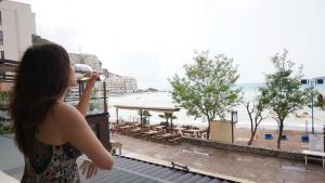 a woman drinking a glass of wine looking out a window at the beach at Beachfront 2BR Apartment with Balcony and Sea View, Biser Mora in Rafailovici +13 photos