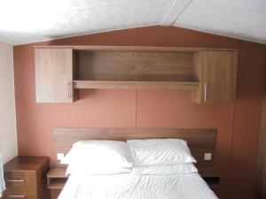 um quarto com uma cama e armários de madeira em Kingfisher : Seabreeze:- 6 Berth, Enclosed veranda, Close to site shop em Ingoldmells